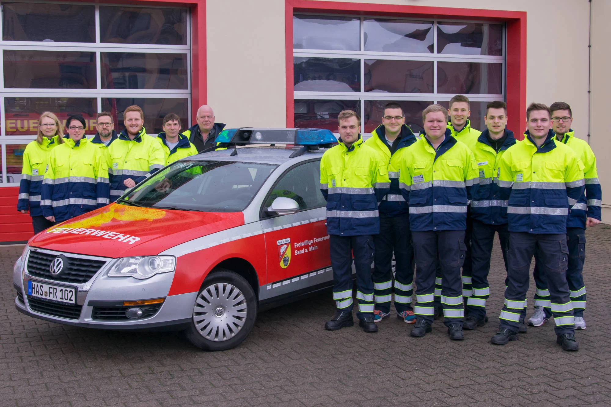 Gruppenfoto der First Responder in Warnjacken neben ihrem Fahrzeug vor dem Feuerwehrhaus